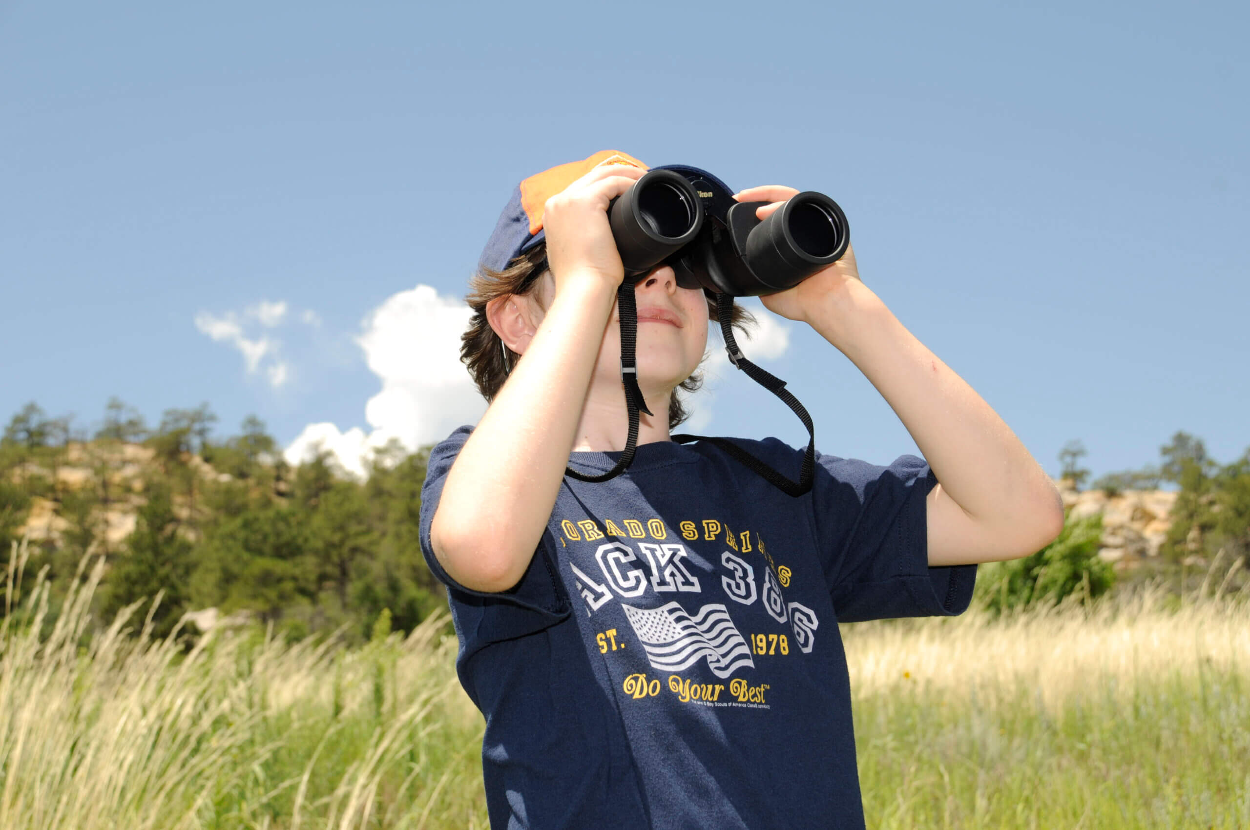 Cub scout standing in a field looking through binoculars